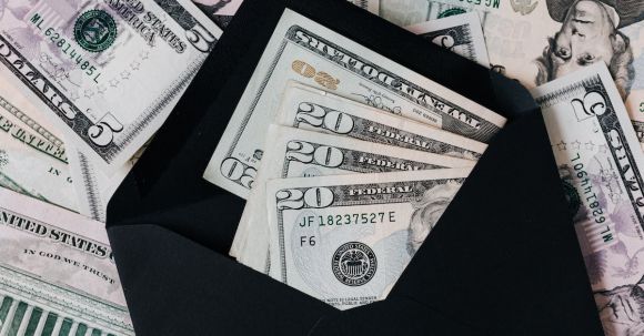 Personal Investing - From above of dollar bills in opened black envelope placed on stack of United states cash money as concept of personal income