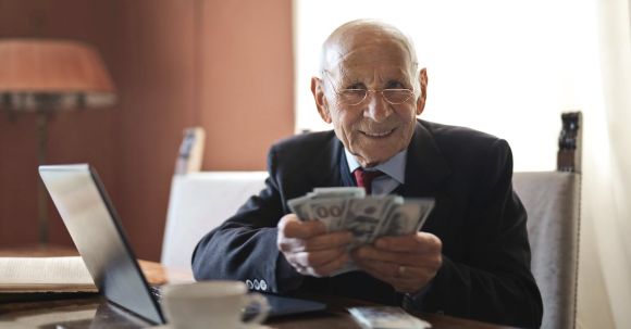 Smart Investing - Confident senior businessman holding money in hands while sitting at table near laptop